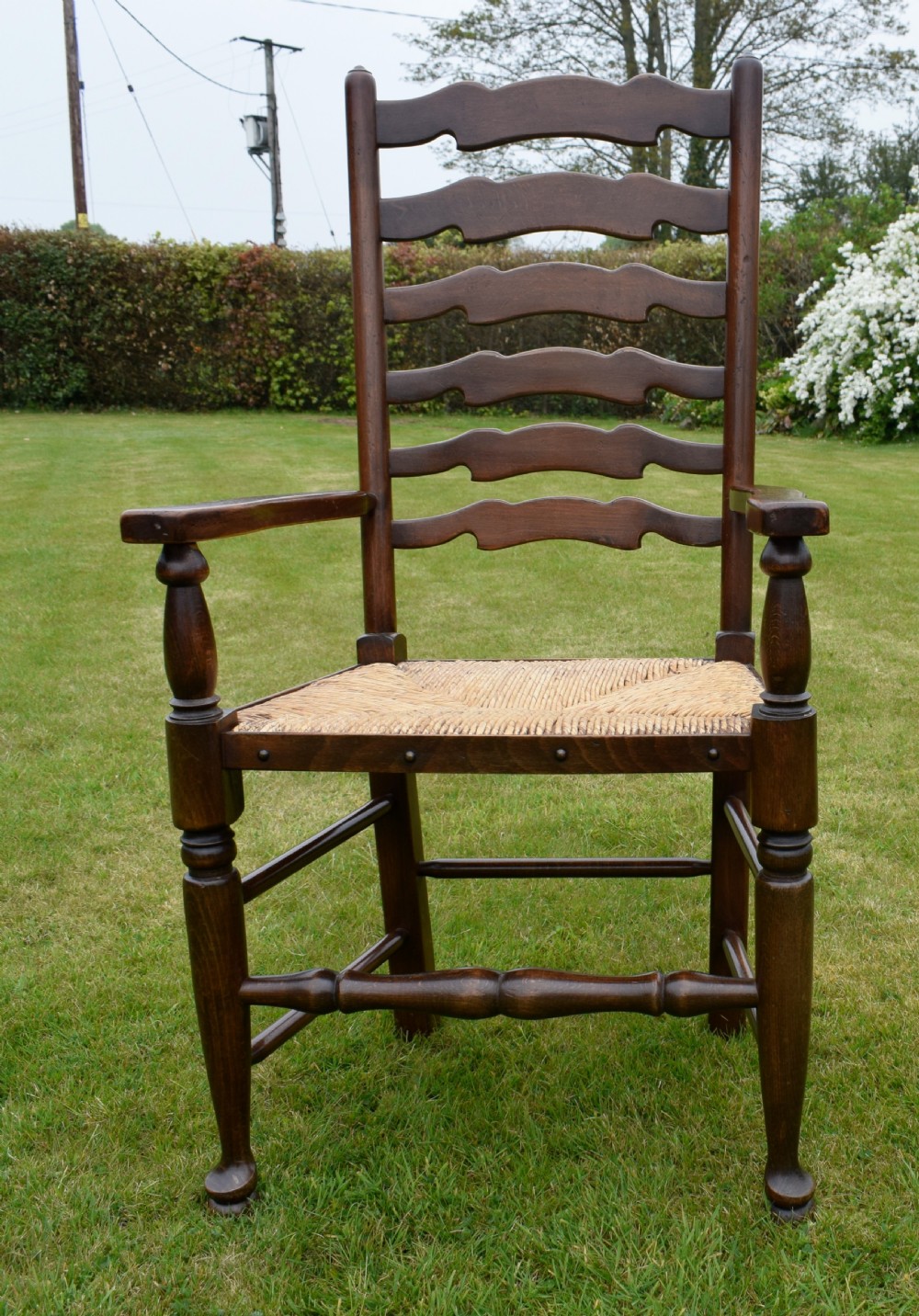 A pair of dark oak ladder back armchairs featuring woven rush seats, curved armrests, and turned front legs. View XX