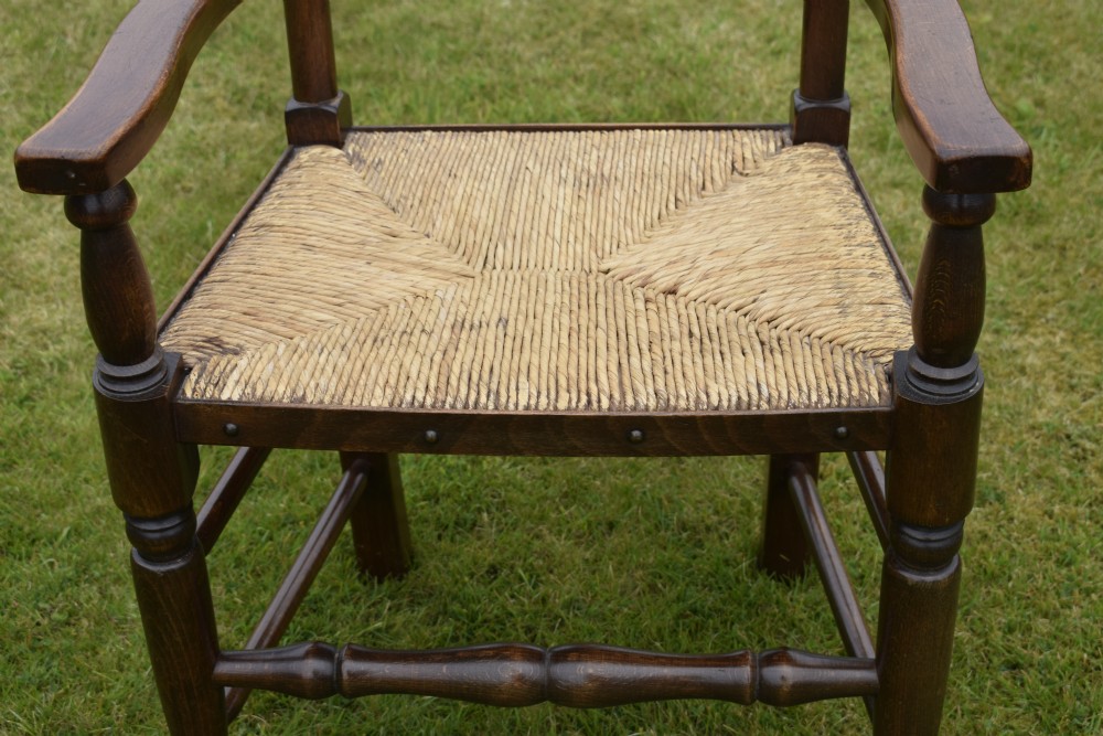 A pair of dark oak ladder back armchairs featuring woven rush seats, curved armrests, and turned front legs. View XXI