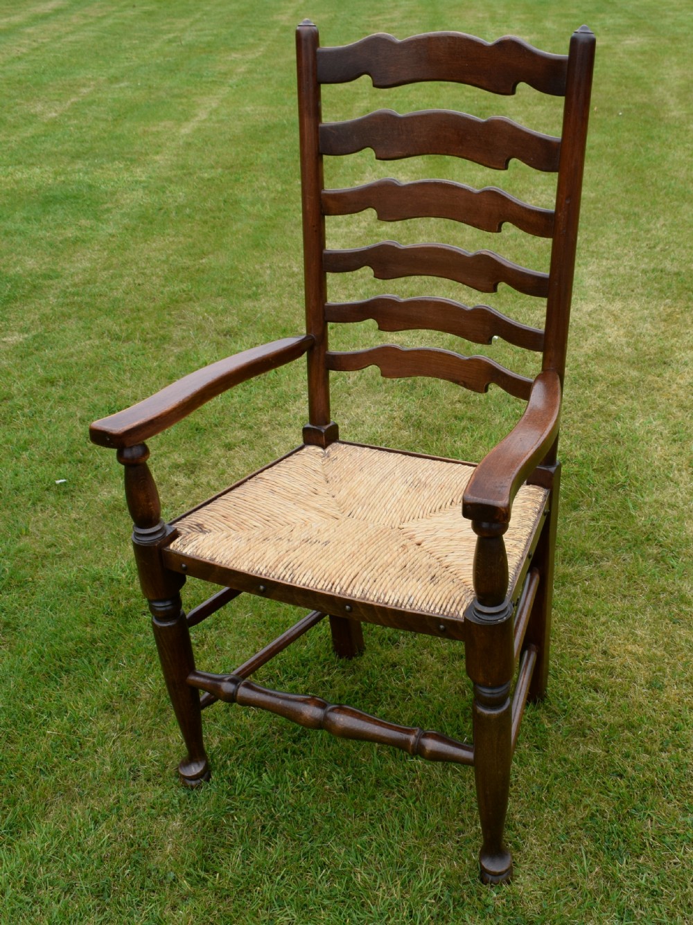 A pair of dark oak ladder back armchairs featuring woven rush seats, curved armrests, and turned front legs. View XXII