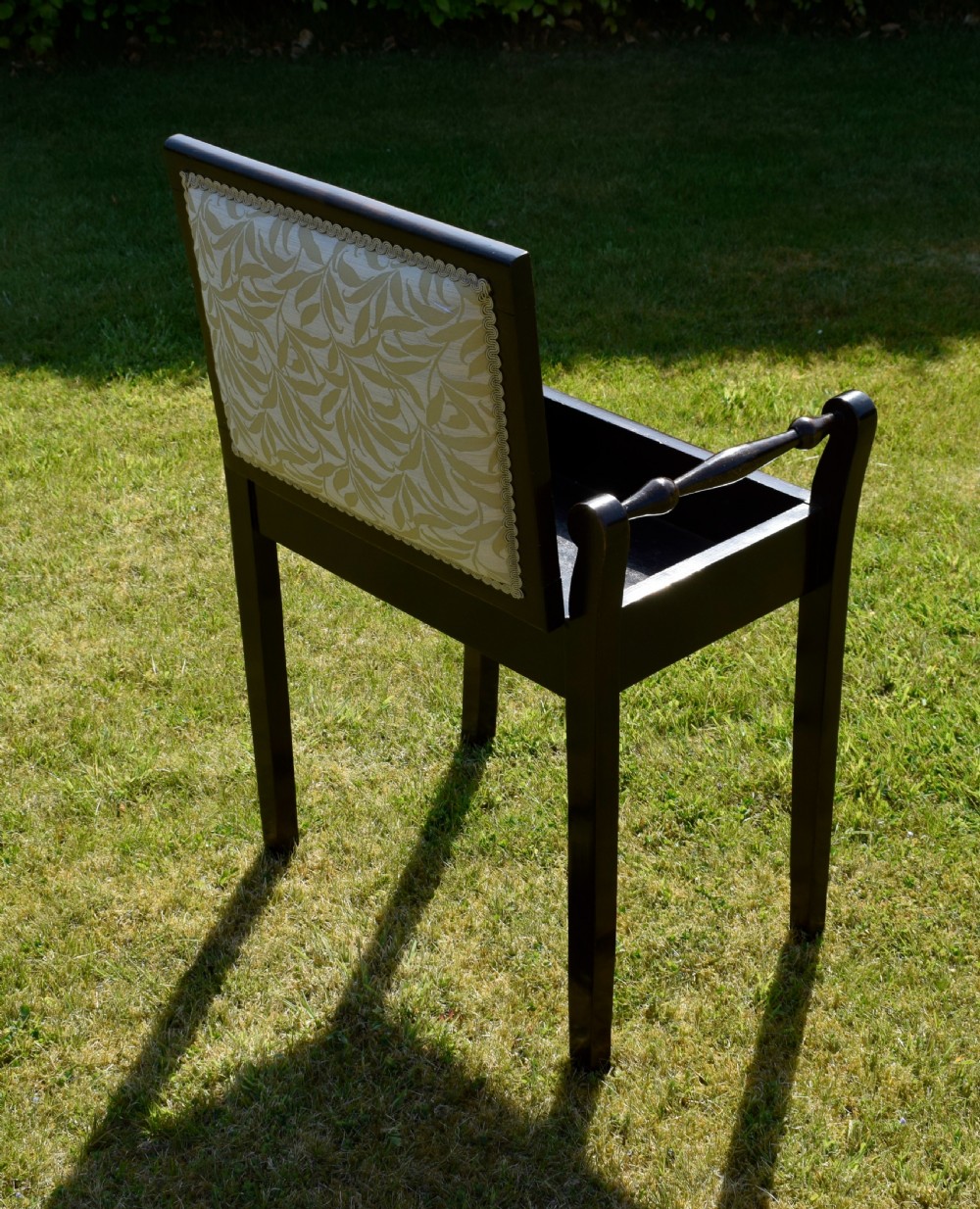 An Edwardian dark mahogany music stool featuring turned side handles, a geometric floral marquetry inlay on the frame, straight tapered legs, and a cream upholstered padded seat. View XII