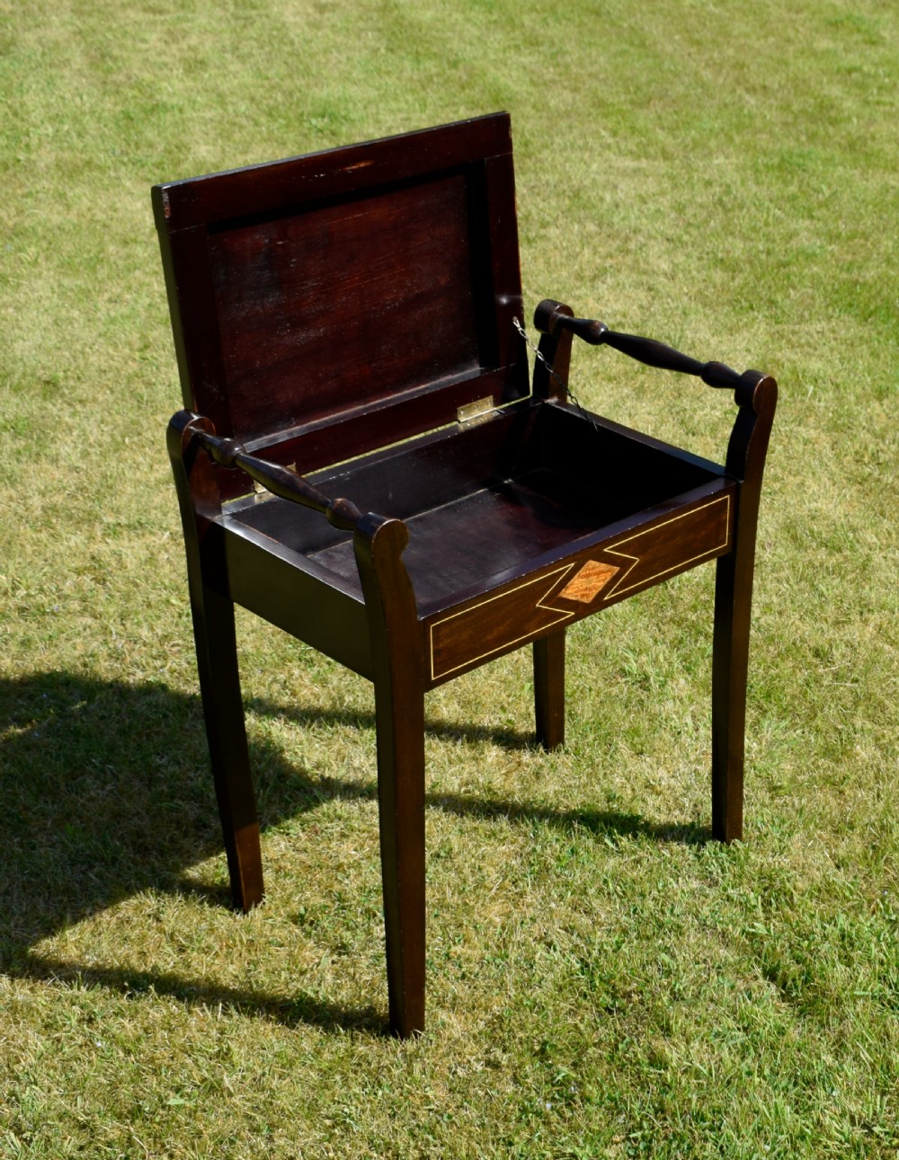 An Edwardian dark mahogany music stool featuring turned side handles, a geometric floral marquetry inlay on the frame, straight tapered legs, and a cream upholstered padded seat. View XIII