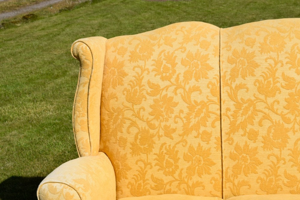 An early 20th-century Georgian style three-seater settee upholstered in yellow floral damask fabric with a serpentine crest back and scrolled arms. View X