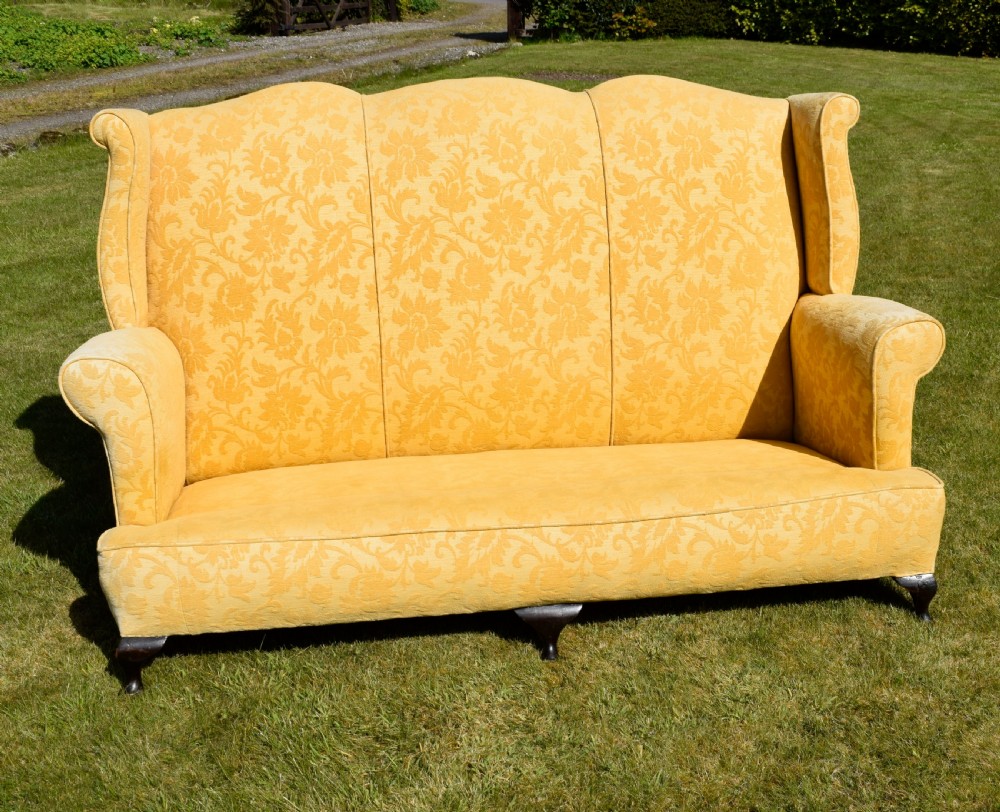 An early 20th-century Georgian style three-seater settee upholstered in yellow floral damask fabric with a serpentine crest back and scrolled arms. View XX