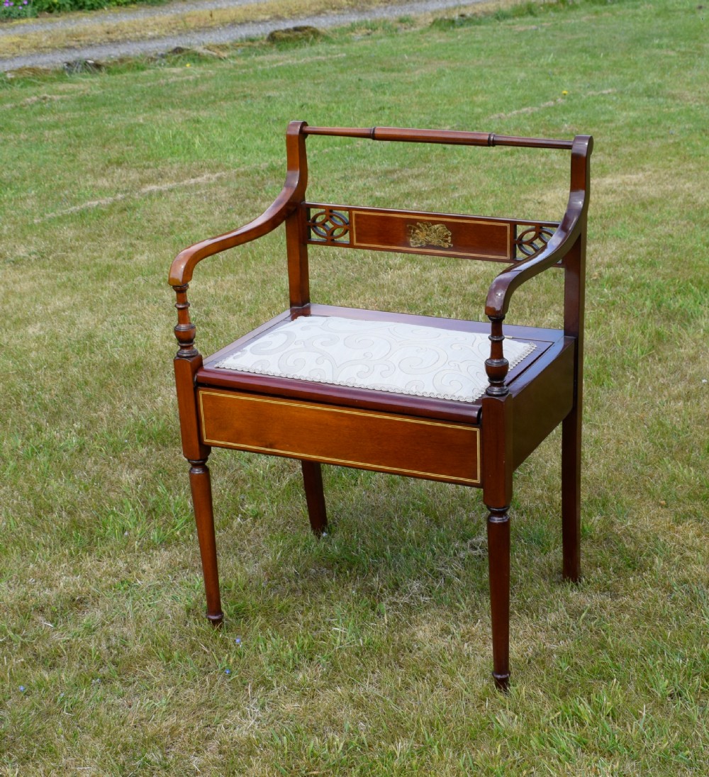 An Edwardian mahogany piano stool featuring marquetry inlay on the backrest, turned side handles, cream patterned upholstered lift-top seat, and tapered legs.