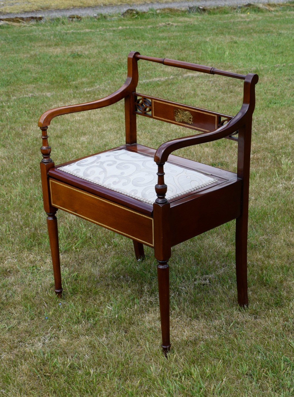 An Edwardian mahogany piano stool featuring marquetry inlay on the backrest, turned side handles, cream patterned upholstered lift-top seat, and tapered legs. View II