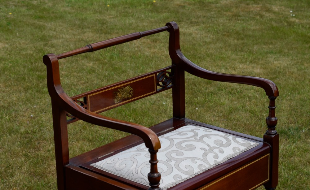 An Edwardian mahogany piano stool featuring marquetry inlay on the backrest, turned side handles, cream patterned upholstered lift-top seat, and tapered legs. View V
