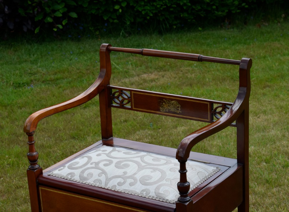 An Edwardian mahogany piano stool featuring marquetry inlay on the backrest, turned side handles, cream patterned upholstered lift-top seat, and tapered legs. View VI