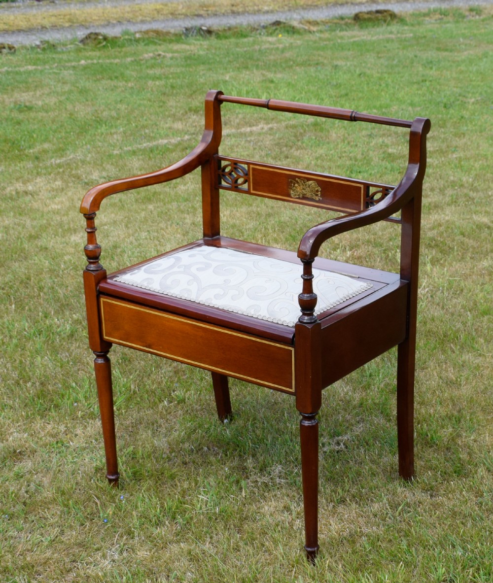 An Edwardian mahogany piano stool featuring marquetry inlay on the backrest, turned side handles, cream patterned upholstered lift-top seat, and tapered legs. View XI