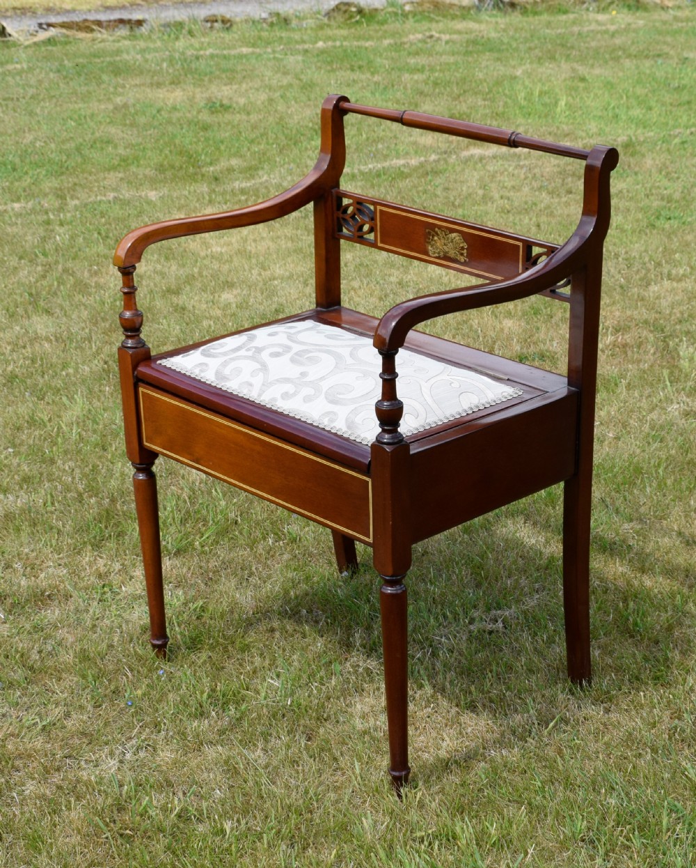An Edwardian mahogany piano stool featuring marquetry inlay on the backrest, turned side handles, cream patterned upholstered lift-top seat, and tapered legs. View XIII