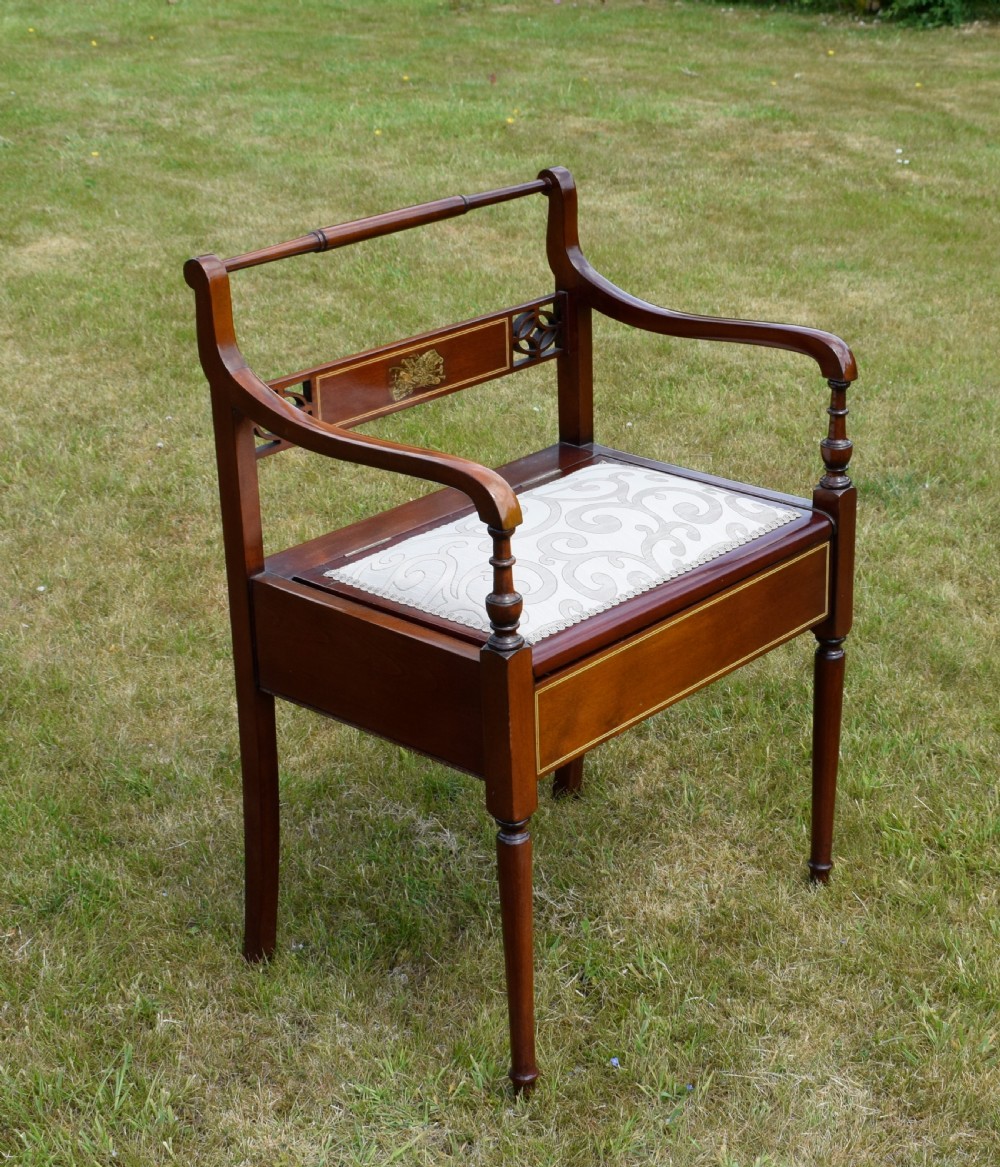 An Edwardian mahogany piano stool featuring marquetry inlay on the backrest, turned side handles, cream patterned upholstered lift-top seat, and tapered legs. View XV