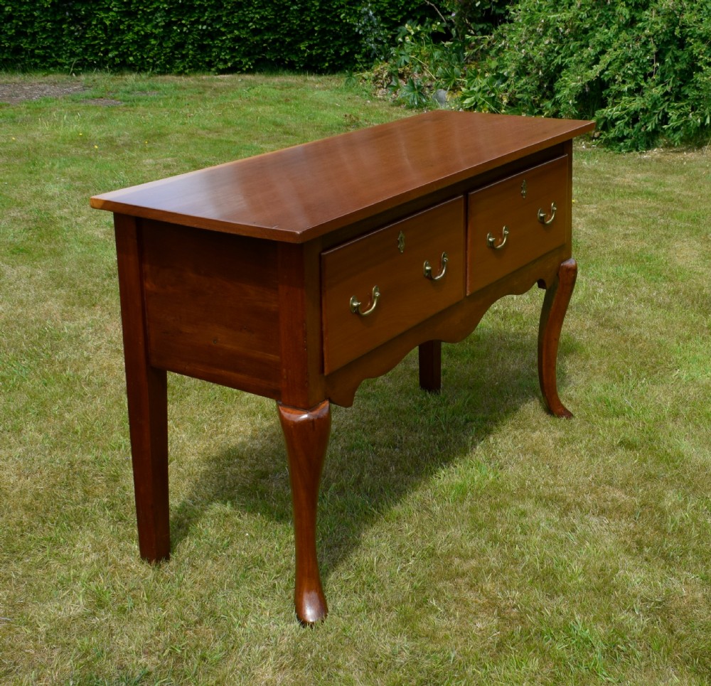 An antique mahogany dresser base featuring two drawers with brass handles, a scalloped apron, and front cabriole legs ending in pad feet.
