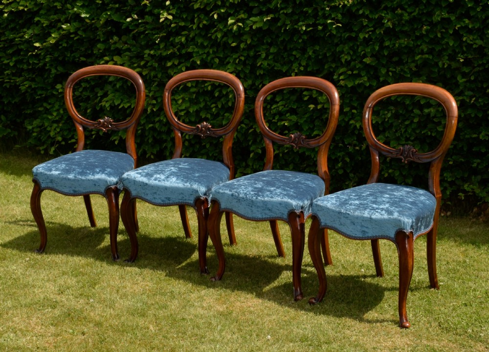 A set of four Victorian balloon back dining chairs crafted from polished walnut with blue velvet upholstered seats and carved crossbars above cabriole front legs. View II