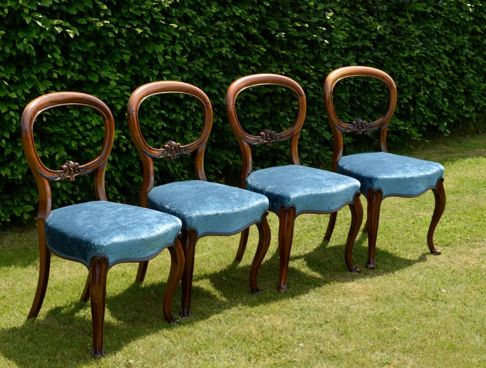 A set of four Victorian balloon back dining chairs crafted from polished walnut with blue velvet upholstered seats and carved crossbars above cabriole front legs. View VI