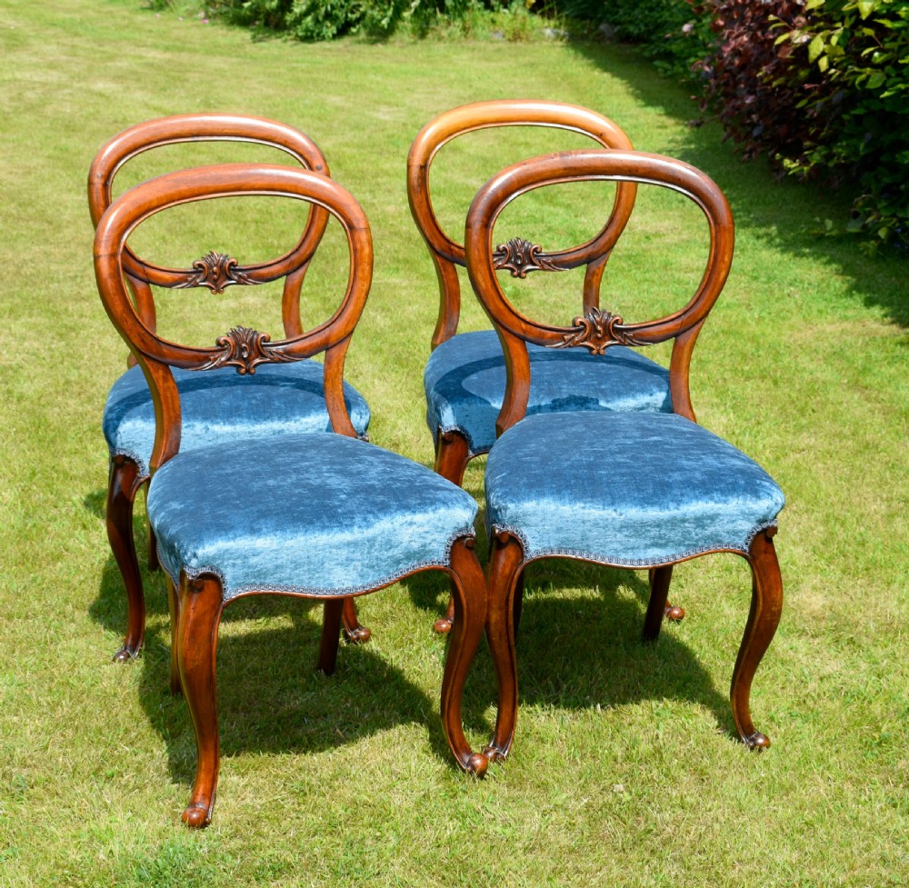 A set of four Victorian balloon back dining chairs crafted from polished walnut with blue velvet upholstered seats and carved crossbars above cabriole front legs. View X