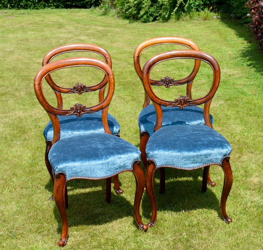 A set of four Victorian balloon back dining chairs crafted from polished walnut with blue velvet upholstered seats and carved crossbars above cabriole front legs. View XI
