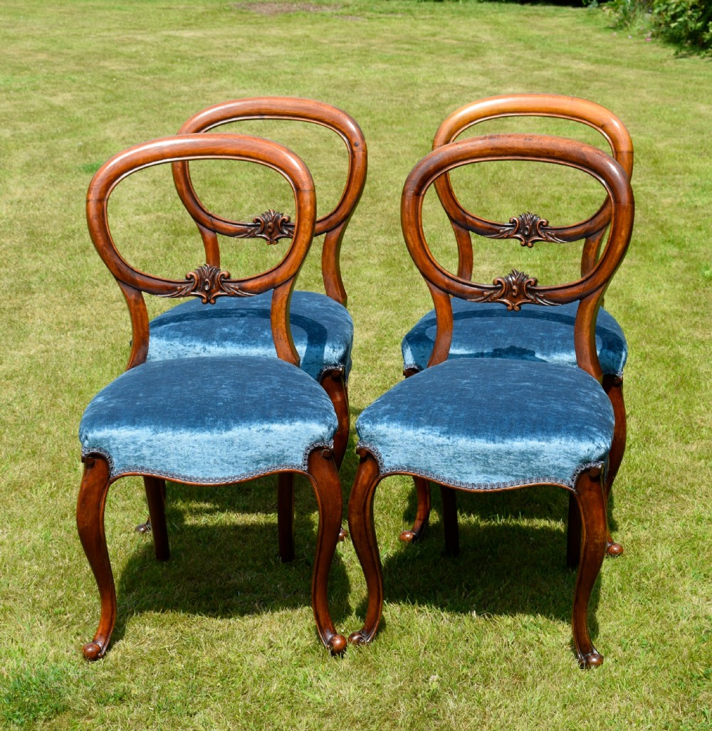 A set of four Victorian balloon back dining chairs crafted from polished walnut with blue velvet upholstered seats and carved crossbars above cabriole front legs. View XII
