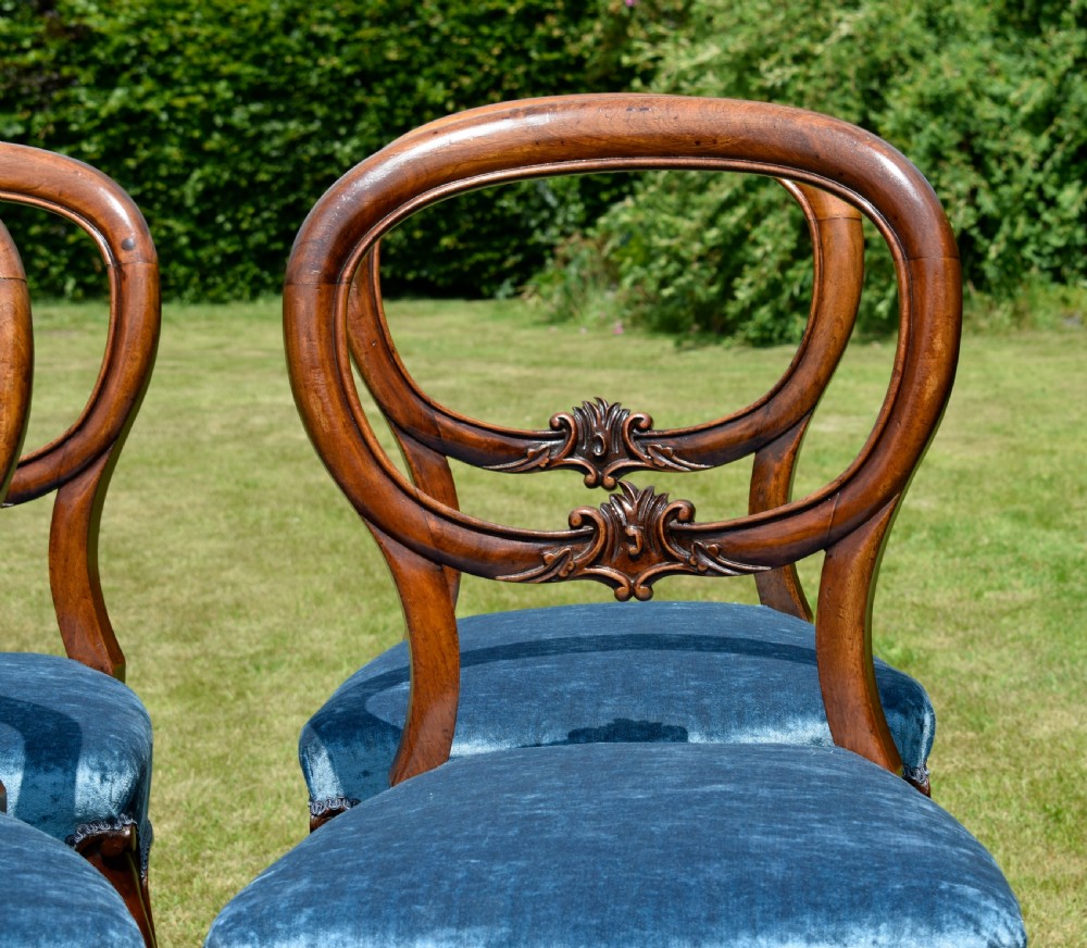 A set of four Victorian balloon back dining chairs crafted from polished walnut with blue velvet upholstered seats and carved crossbars above cabriole front legs. View XIII