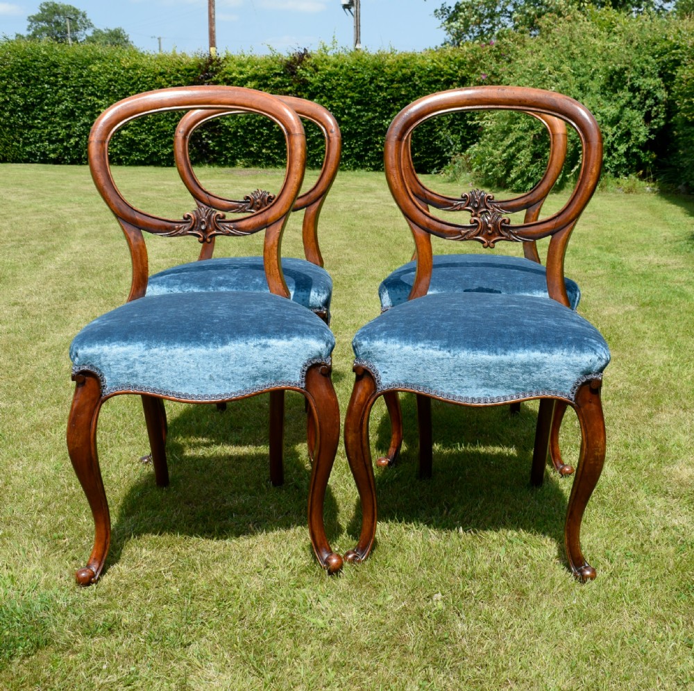 A set of four Victorian balloon back dining chairs crafted from polished walnut with blue velvet upholstered seats and carved crossbars above cabriole front legs. View XIV