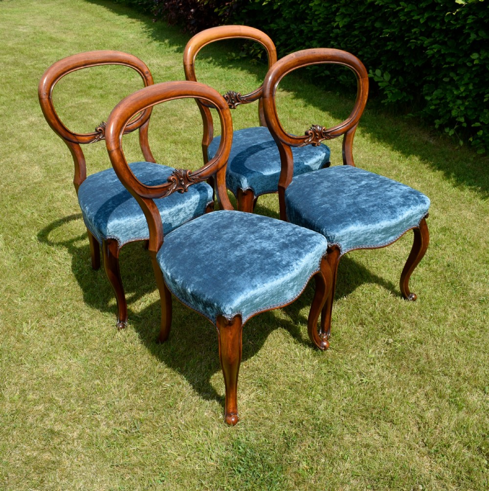 A set of four Victorian balloon back dining chairs crafted from polished walnut with blue velvet upholstered seats and carved crossbars above cabriole front legs. View XV