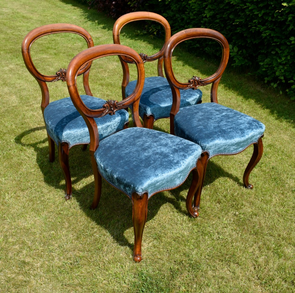A set of four Victorian balloon back dining chairs crafted from polished walnut with blue velvet upholstered seats and carved crossbars above cabriole front legs. View XVI