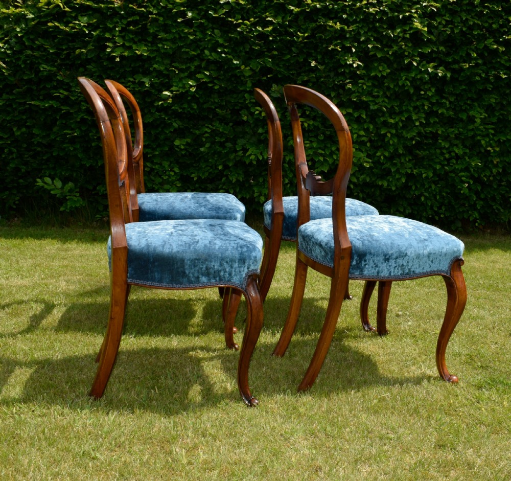 A set of four Victorian balloon back dining chairs crafted from polished walnut with blue velvet upholstered seats and carved crossbars above cabriole front legs. View XVII