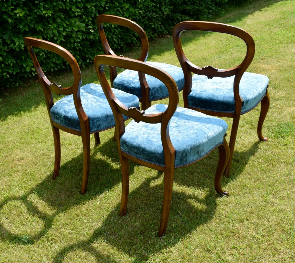 A set of four Victorian balloon back dining chairs crafted from polished walnut with blue velvet upholstered seats and carved crossbars above cabriole front legs. View XVIII