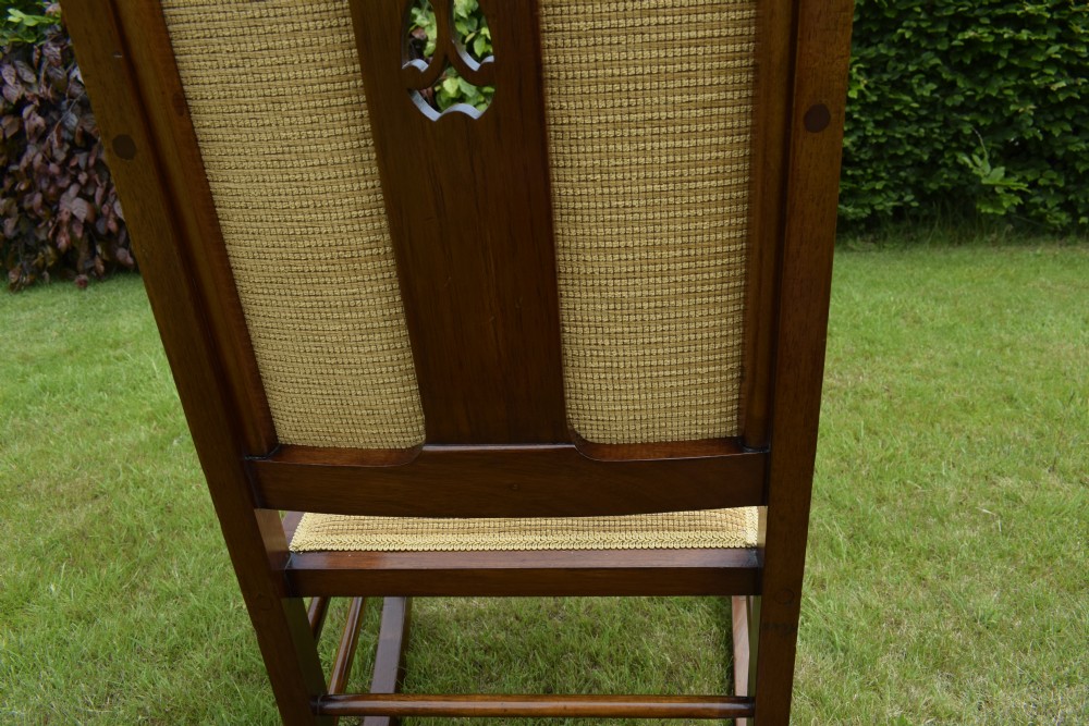 An Edwardian mahogany rocking chair featuring a crest rail with central marquetry inlay, double upholstered back panels, pierced fretwork splats, and light beige textured upholstery. View VIII