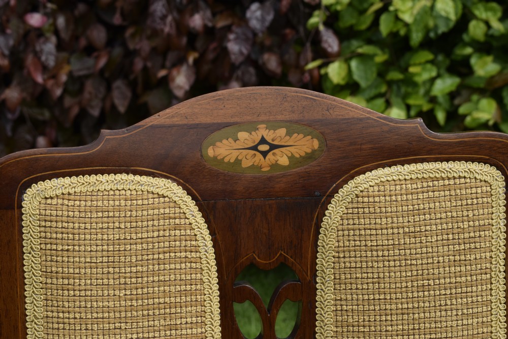 An Edwardian mahogany rocking chair featuring a crest rail with central marquetry inlay, double upholstered back panels, pierced fretwork splats, and light beige textured upholstery. View XIII