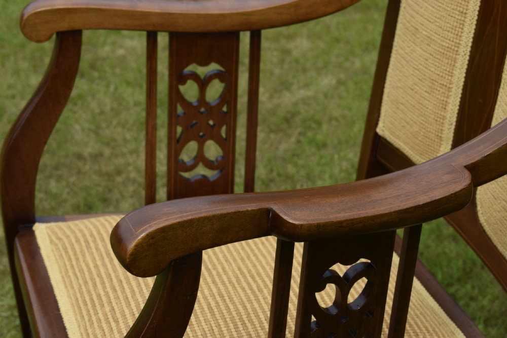 An Edwardian mahogany rocking chair featuring a crest rail with central marquetry inlay, double upholstered back panels, pierced fretwork splats, and light beige textured upholstery. View XX