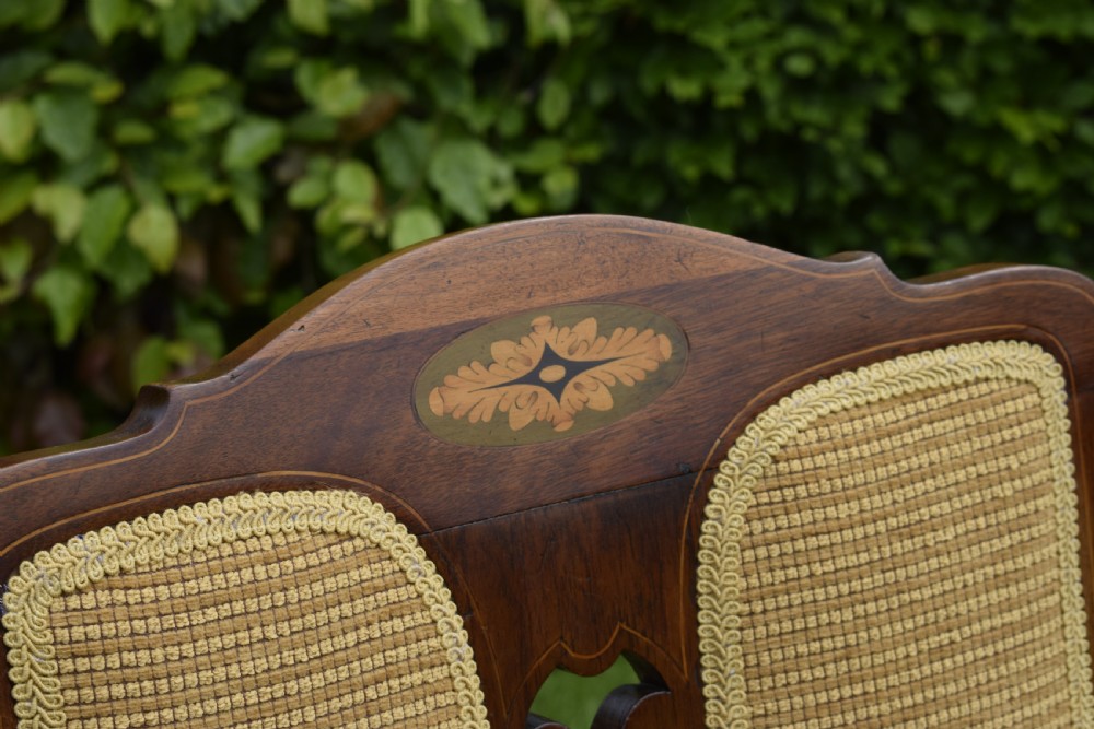 An Edwardian mahogany rocking chair featuring a crest rail with central marquetry inlay, double upholstered back panels, pierced fretwork splats, and light beige textured upholstery. View XXIII