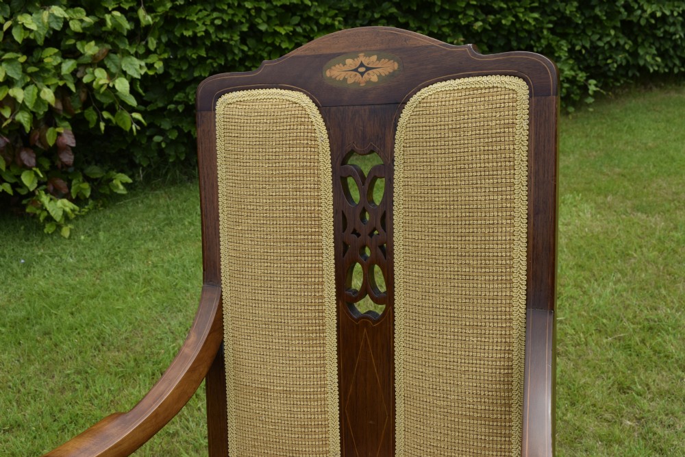 An Edwardian mahogany rocking chair featuring a crest rail with central marquetry inlay, double upholstered back panels, pierced fretwork splats, and light beige textured upholstery. View XXVII