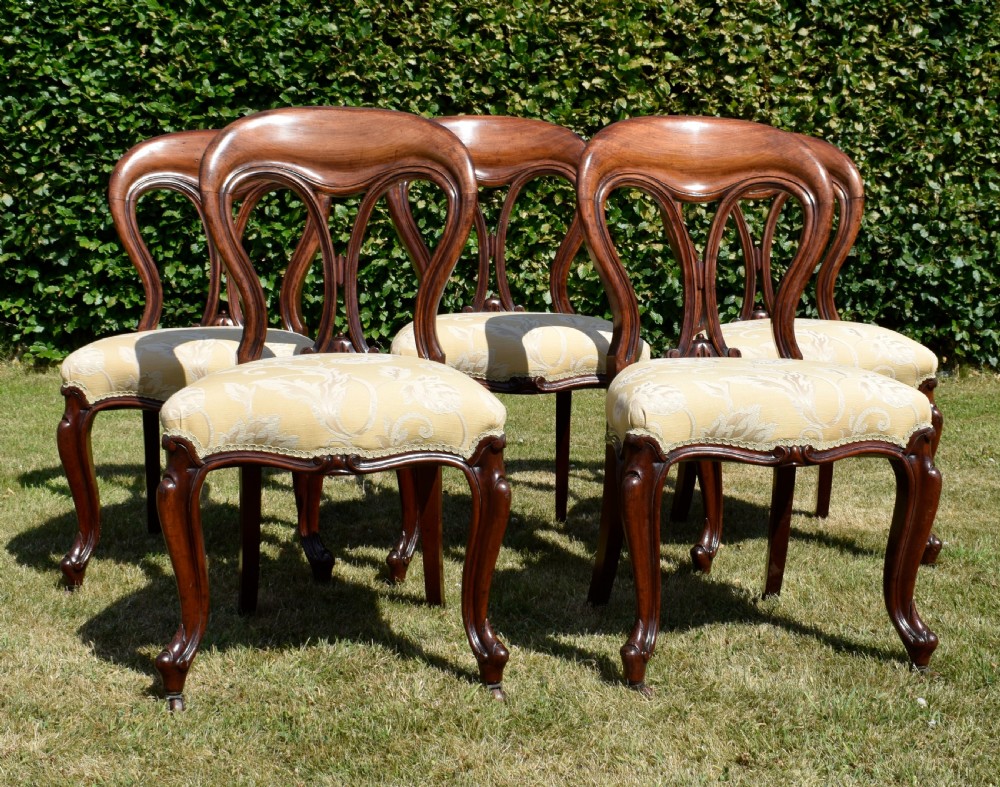 A set of five Victorian mahogany balloon back dining chairs with carved cabriole front legs and pale cream pattern-upholstered seats. View VI