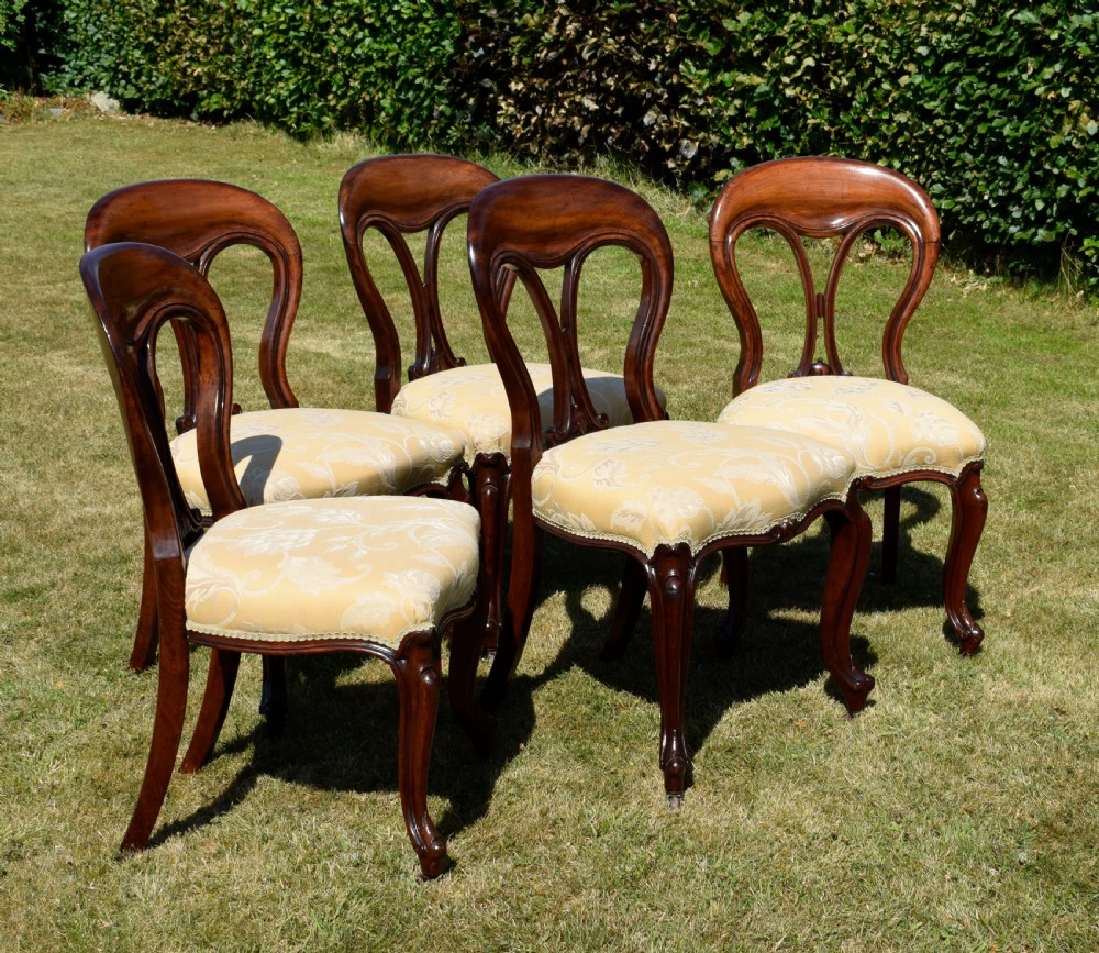 A set of five Victorian mahogany balloon back dining chairs with carved cabriole front legs and pale cream pattern-upholstered seats. View XI