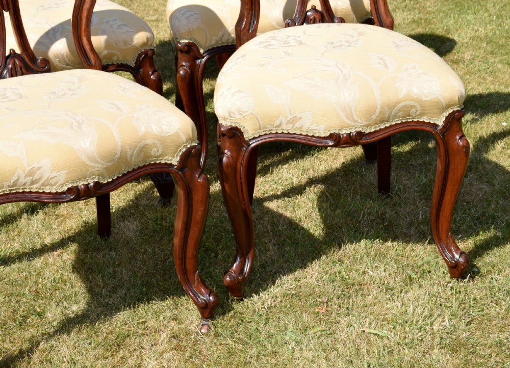 A set of five Victorian mahogany balloon back dining chairs with carved cabriole front legs and pale cream pattern-upholstered seats. View XV