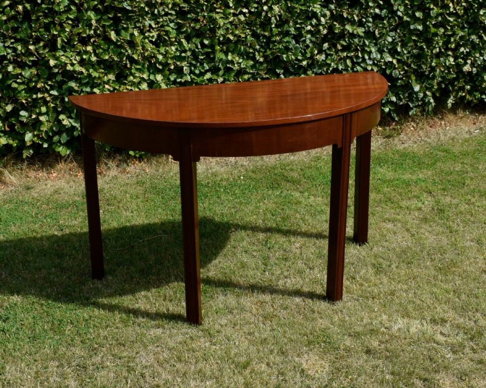 A Georgian mahogany demi-lune console table featuring a semi-circular top and four tapered legs.