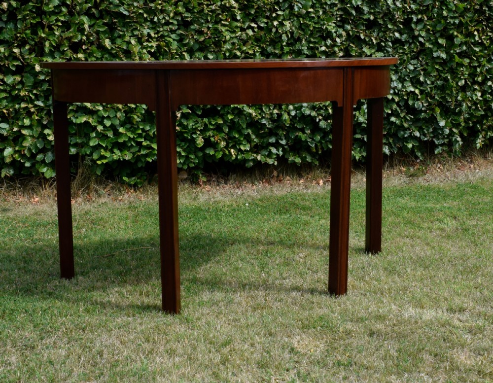 A Georgian mahogany demi-lune console table featuring a semi-circular top and four tapered legs. View V