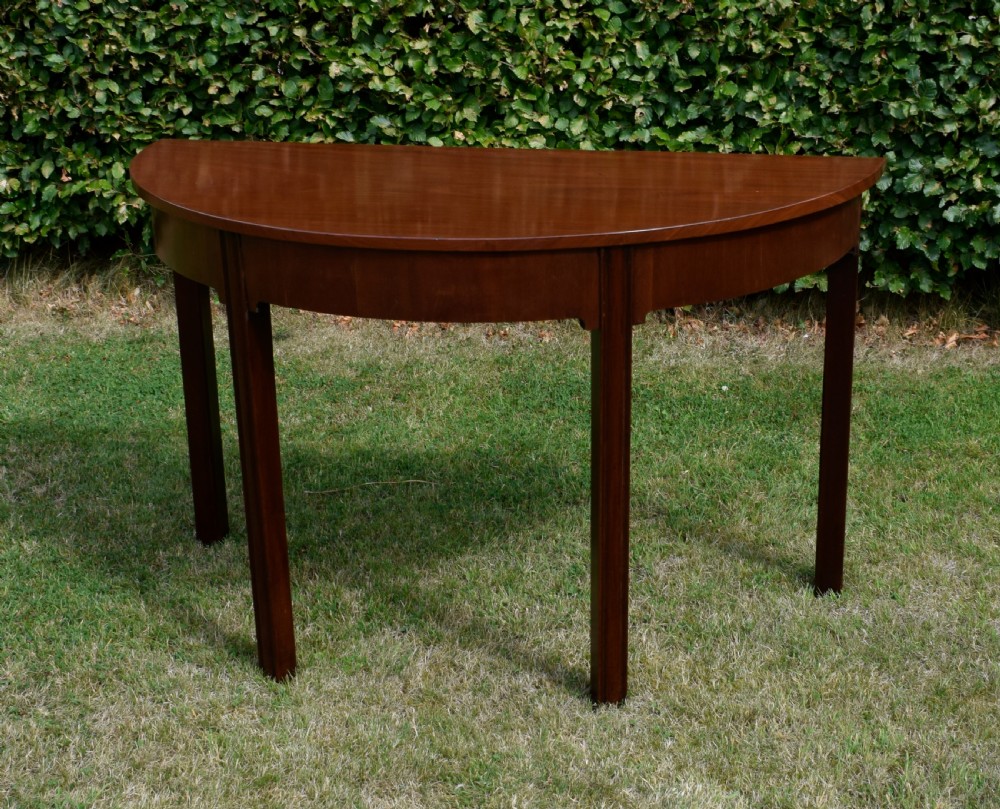 A Georgian mahogany demi-lune console table featuring a semi-circular top and four tapered legs. View VII