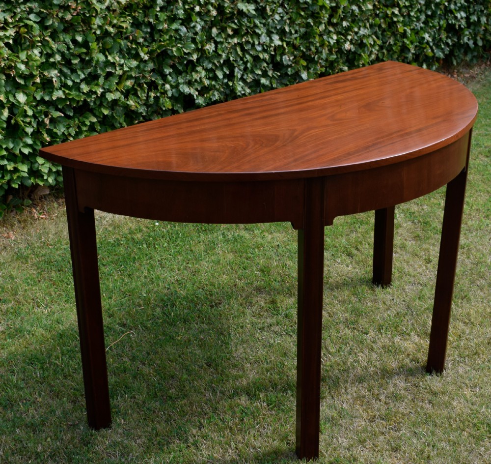 A Georgian mahogany demi-lune console table featuring a semi-circular top and four tapered legs. View IX