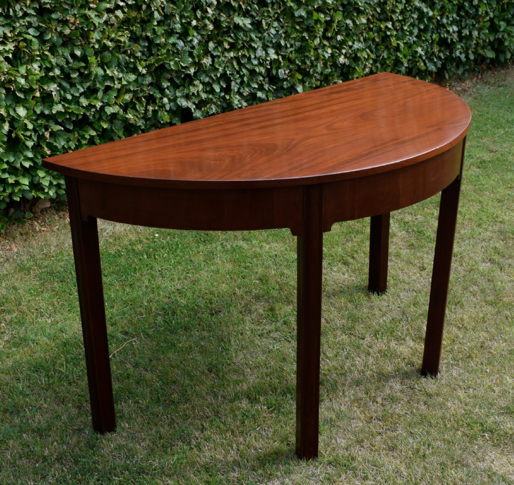 A Georgian mahogany demi-lune console table featuring a semi-circular top and four tapered legs. View X