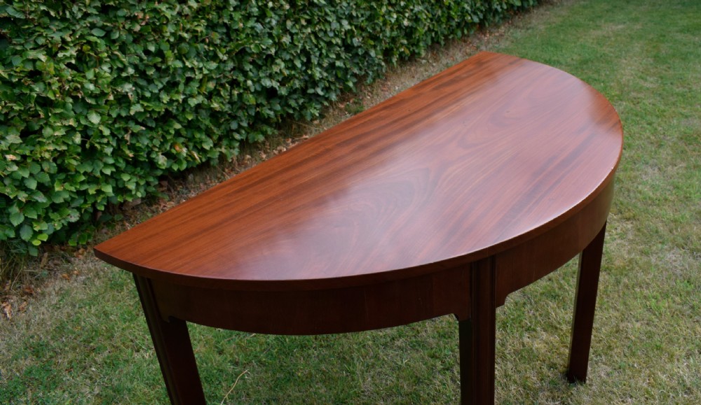 A Georgian mahogany demi-lune console table featuring a semi-circular top and four tapered legs. View XVI