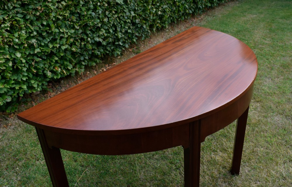 A Georgian mahogany demi-lune console table featuring a semi-circular top and four tapered legs. View XVIII