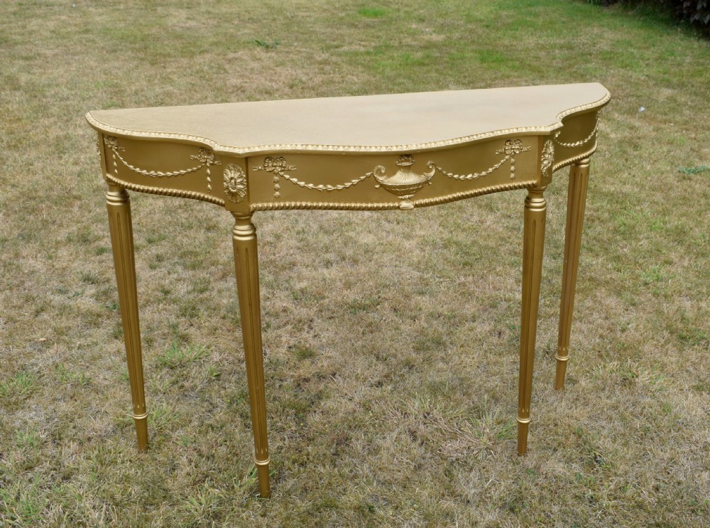 A gold gilded early twentieth-century console table featuring carved swags, a central urn motif, and fluted tapered legs.