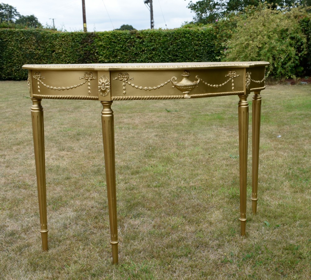 A gold gilded early twentieth-century console table featuring carved swags, a central urn motif, and fluted tapered legs. View V