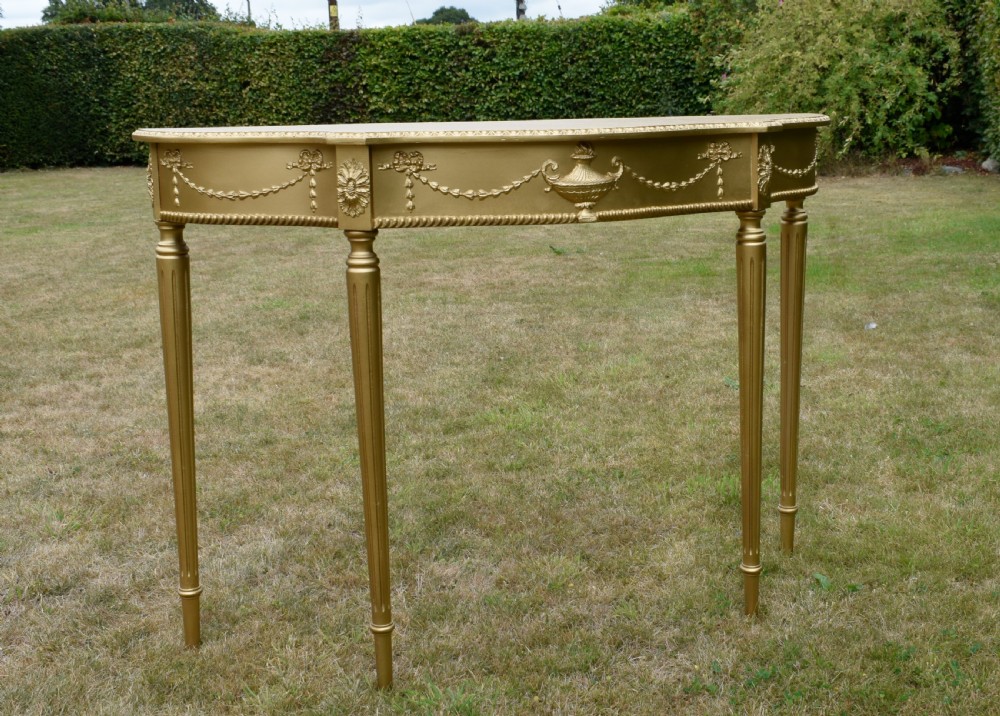 A gold gilded early twentieth-century console table featuring carved swags, a central urn motif, and fluted tapered legs. View VI