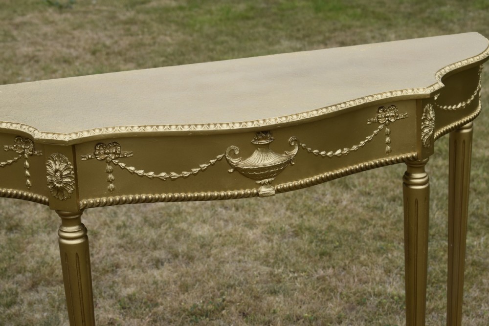 A gold gilded early twentieth-century console table featuring carved swags, a central urn motif, and fluted tapered legs. View IX