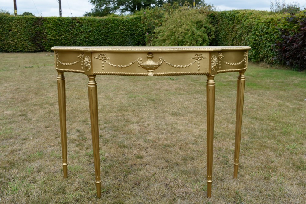 A gold gilded early twentieth-century console table featuring carved swags, a central urn motif, and fluted tapered legs. View X