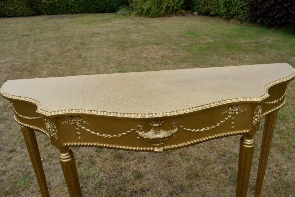 A gold gilded early twentieth-century console table featuring carved swags, a central urn motif, and fluted tapered legs. View XV