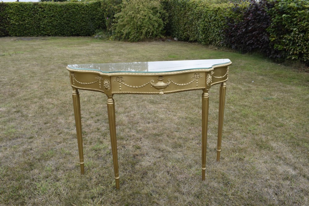 A gold gilded early twentieth-century console table featuring carved swags, a central urn motif, and fluted tapered legs. View XX