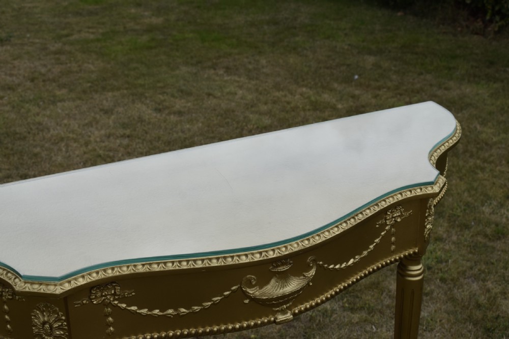 A gold gilded early twentieth-century console table featuring carved swags, a central urn motif, and fluted tapered legs. View XXI