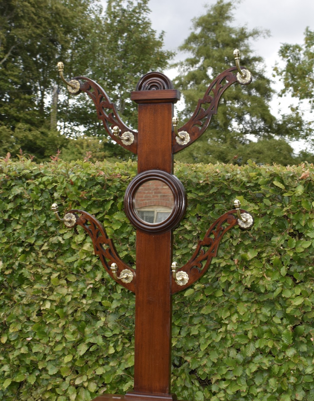 A Victorian walnut hall stand featuring carved fretwork branches, brass coat hooks, a central circular mirror, a glove box, and a lower drip tray base. View II
